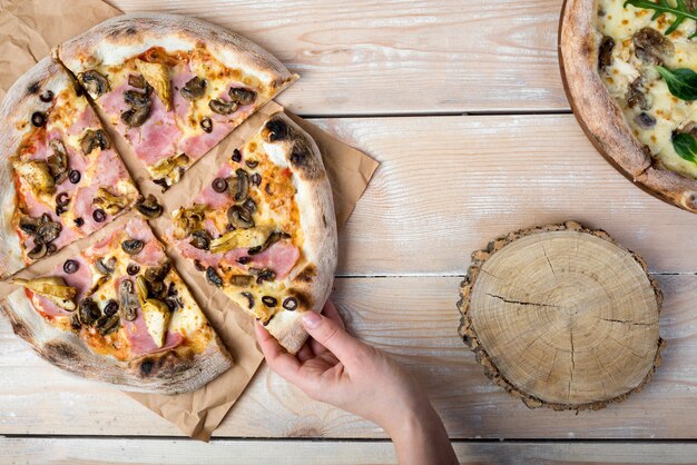 Human hand holding tasty mushroom and bacon pizza on textured wooden plank