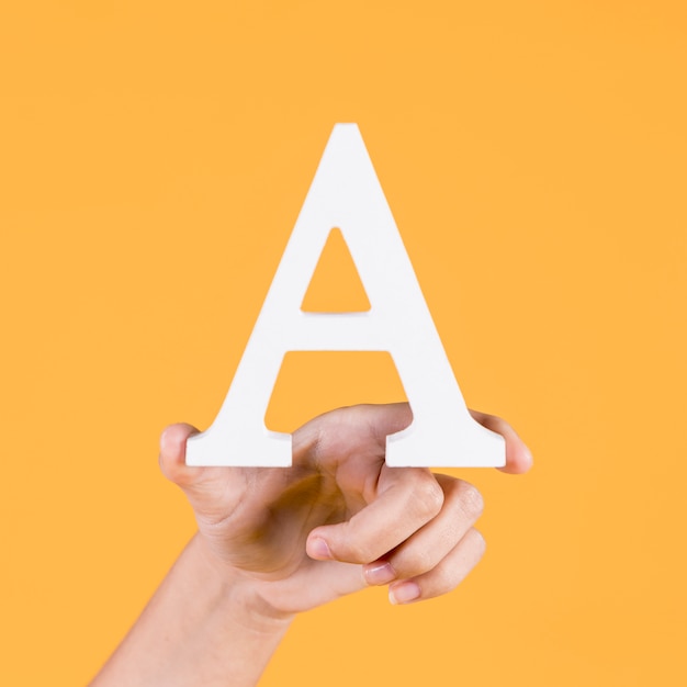 Free photo human hand holding up the uppercase capital letter a over yellow background