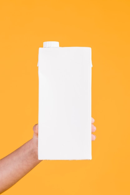 Human hand holding white milk box on yellow background