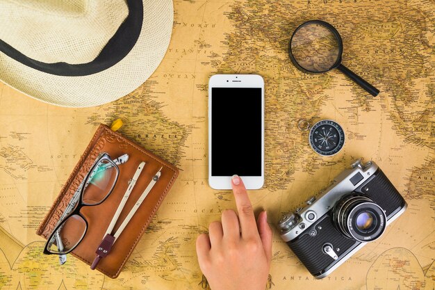 Human hand on mobile phone with travelling equipments around on map