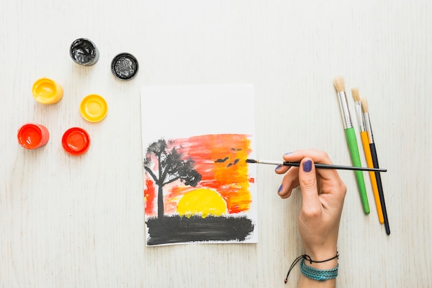 Human hand painting a beautiful nature sunset seen on paper with water colors