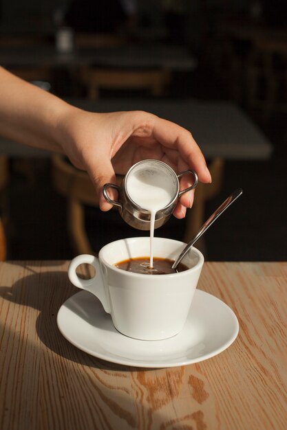 Human hand pouring milk into the black coffee in cafeteria