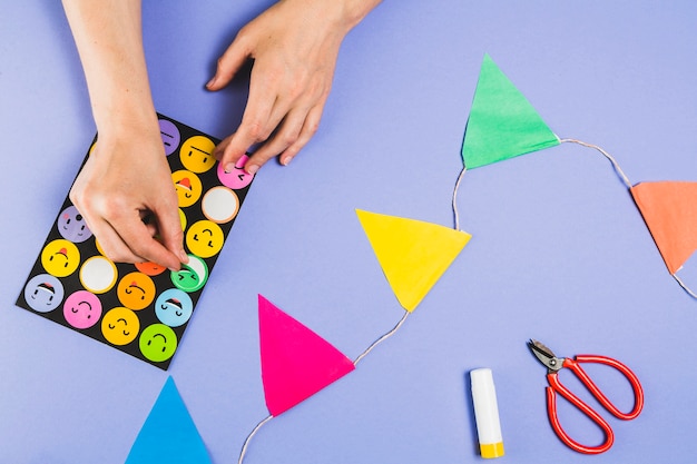 Human hand removing emoji from stickers set for making craft on purple surface