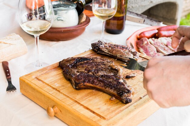 Human hand slicing meat on wooden chopping board