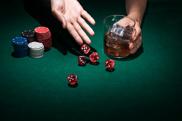Human hand throw red dice while holding glass of whiskey