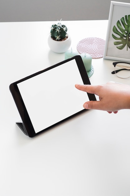 Human hand touching tablet near photo frame and eyeglasses on table