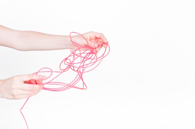 Human hand trying to untangle red wire on white background