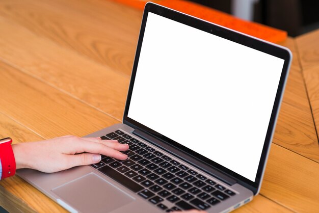 Human hand using laptop with blank white screen over wooden desk