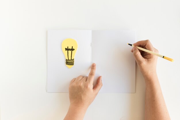 Human hand writing on card with light bulb