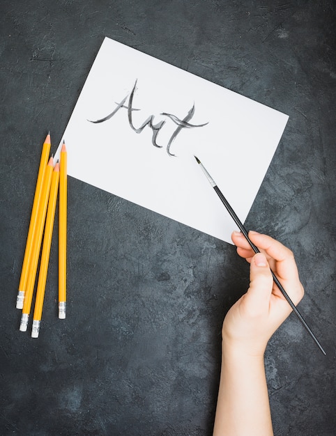 Human hand written art text on white page with paint brush over slate surface