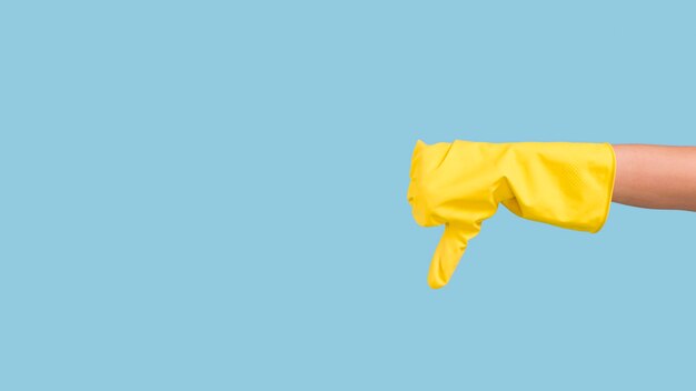 Human hand in yellow glove showing sign of dislike over blue wall