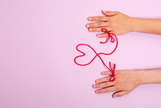 Human hands connected with red thread in heart shape