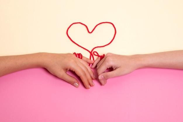 Foto gratuita mani umane collegate con filo rosso a forma di cuore