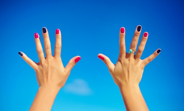 Free photo human hands  with bright colorful nails over blue sky