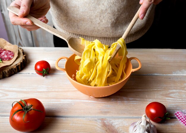 Human hands with wooden spoons mixing boiled spaghetti in colander over kitchen counter