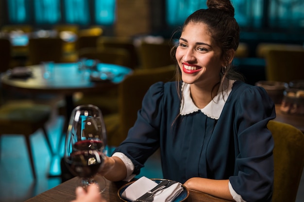 Human and happy woman clanging glasses of wine at table in cafe