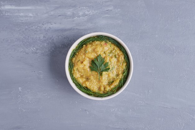 Hummus in a white cup with herbs in the center.