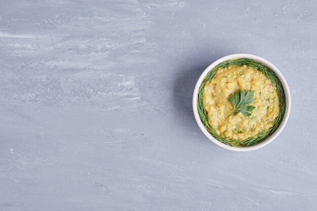 Hummus in a white cup with herbs.