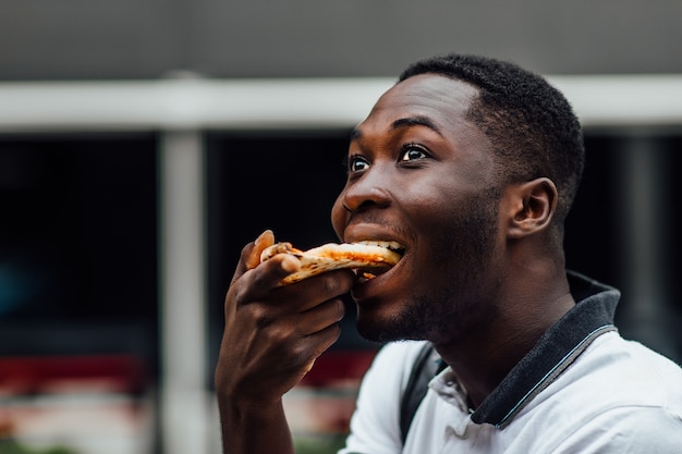 無料写真 空腹のアフリカ人が通りでピザを食べるクローズアップ