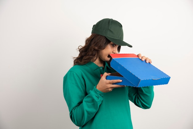 Hungry delivery woman opening pizza box on white.