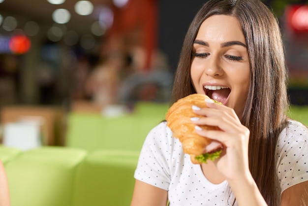 Foto gratuita cornetto mordace femminile affamato nella caffetteria