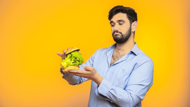 Hungry handsome man holds a hamburger in his hand on yellow background