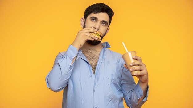 Голодный красавец держит в руке гамбургер на желтом фоне