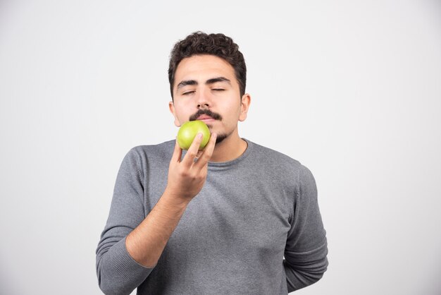 Hungry man smells green apple on gray.