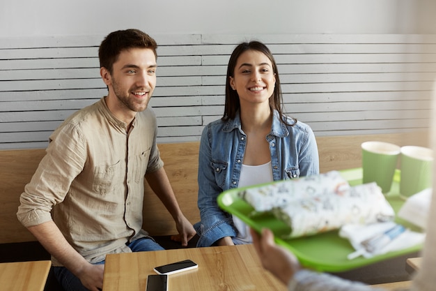 Free photo hungry young couple on a date sitting in cafeteria, spending time together, waiting for waiter brings order with excited about meal.