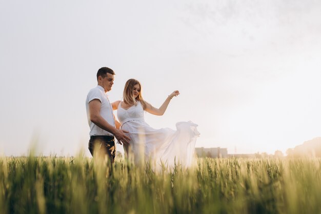 The husband embarcing wife's stomach and standing on the field