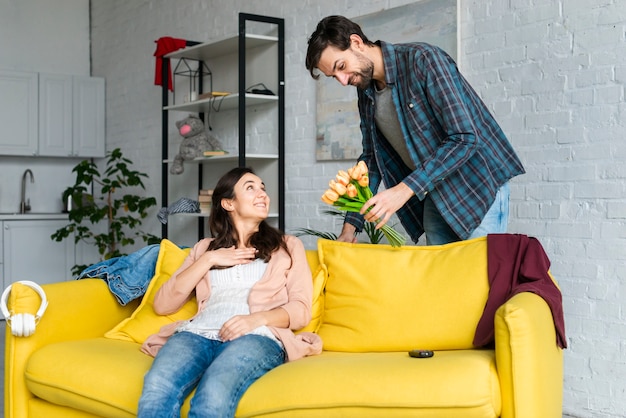 Husband giving flowers to her wife in living room