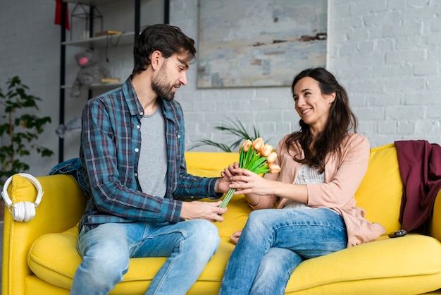 Husband giving flowers to her wife sitting on the couch