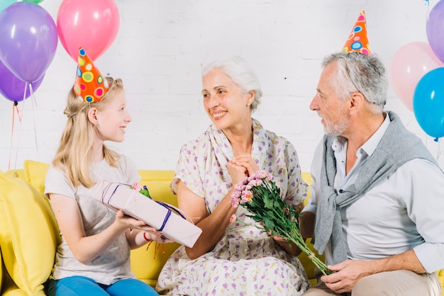 Husband and granddaughter giving birthday gift to happy woman