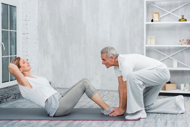 Husband helping his wife with yoga pose on exercise mat