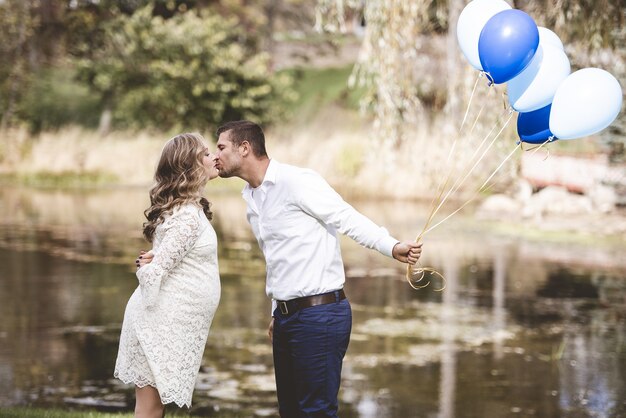 남편이 풍선을 들고 호수가있는 정원에서 임신 한 아내에게 키스