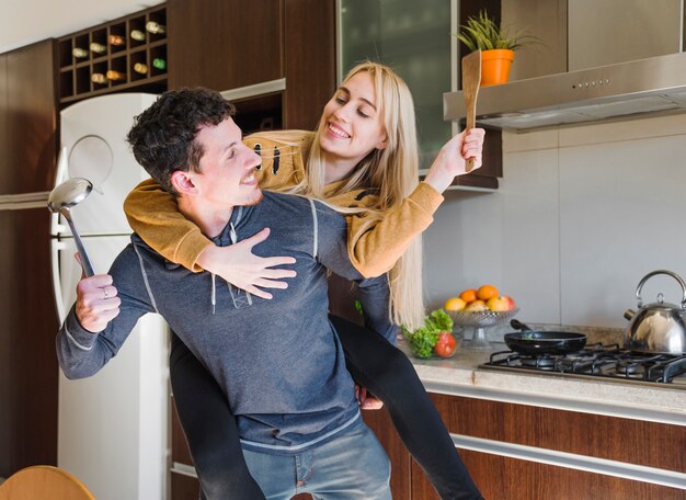 Husband holding ladle and spatula in hand carrying his wife on back