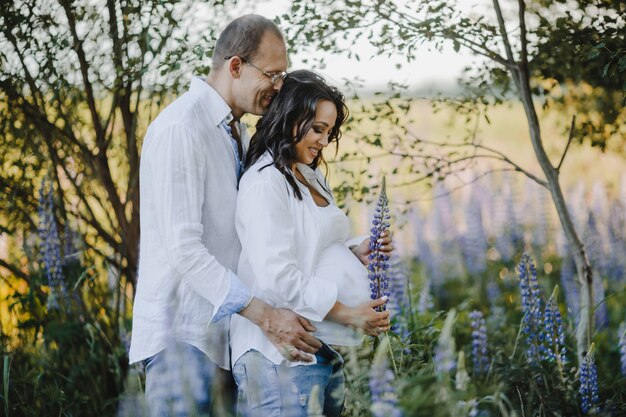 Husband hugs for back his pregnant wife among lupins field