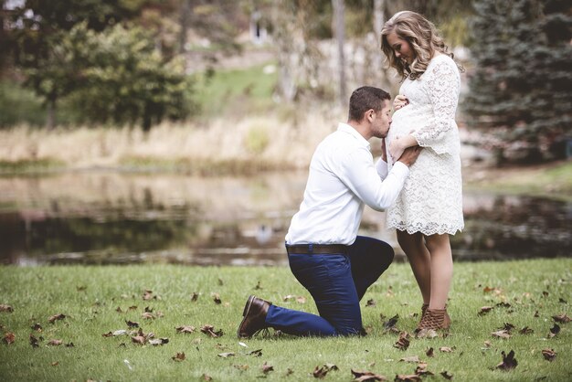 Husband kissing the belly of his pregnant wife in a garden with a lake