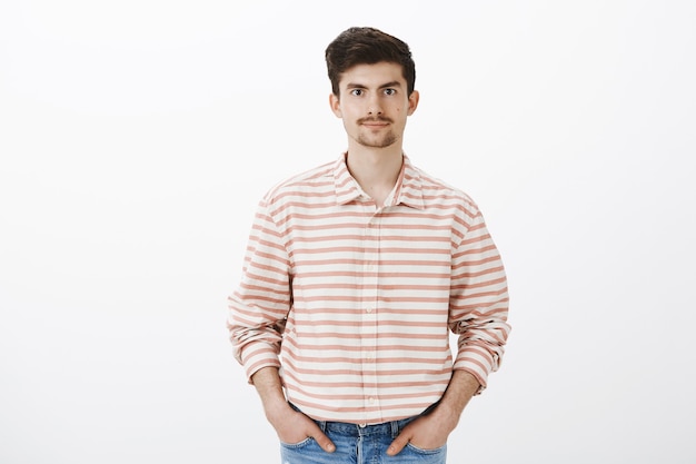 Husband waiting for wife to give grocery list. Mature ordinary european guy with moustache and beard in striped shirt, holding hands in pockets and smiling politely, feeling relaxed and casual