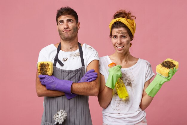 Husband wearing apron and gloves holding sponge looking fatigued up