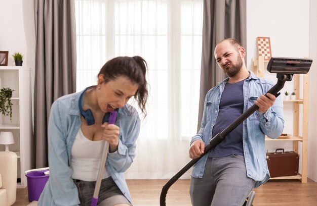 Husband and wife singing together while cleaning apartment