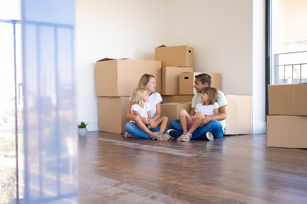 Husband, wife and their daughters sitting on floor and moving in new home