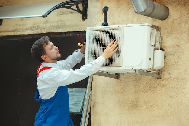 HVAC technician working on a capacitor part for condensing unit. Male worker or repairman in uniform repairing and adjusting conditioning system, diagnosing and looking for technical issues.