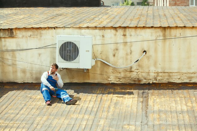 HVAC technician working on a capacitor part for condensing unit. Male worker or repairman in uniform repairing and adjusting conditioning system, diagnosing and looking for technical issues.