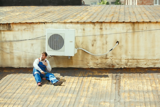 凝縮ユニットのコンデンサ部分に取り組んでいるHVAC技術者。均一な修理とコンディショニングシステムの調整、診断と技術的な問題の検索を行う男性労働者または修理工。