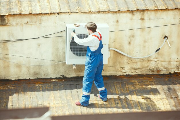 Техник HVAC работает над конденсаторной частью для конденсаторной установки. Мужчина-рабочий или ремонтник в униформе ремонтирует и регулирует систему кондиционирования, диагностирует и ищет технические проблемы.