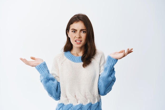 I am confused Clueless and puzzled young woman dont understand raising hands and shrugging shoulders standing indecisive against white background