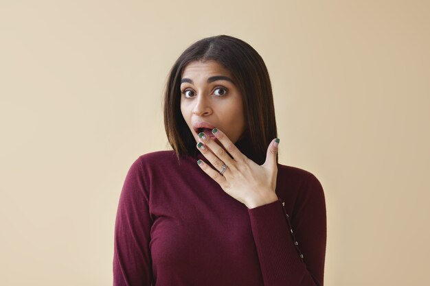 I can't believe this. amazed young dark skinned lady having funny astonished look, covering opened mouth with hand, shocked with intriguing juicy gossip. Human facial expressions