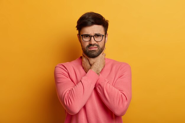 i cannot breath. distressed frustrated unshven guy keeps hands on neck, chokes and feels sore throat, has asthmatic fit, feels discomfort and painful feelings, poses indoor, needs painkillers