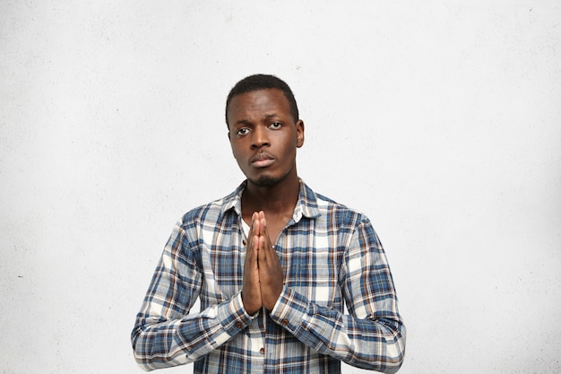 Free photo i did’t mean to hurt your feelings. portrait of unhappy and sad young black man having guilty look, keeping hands together